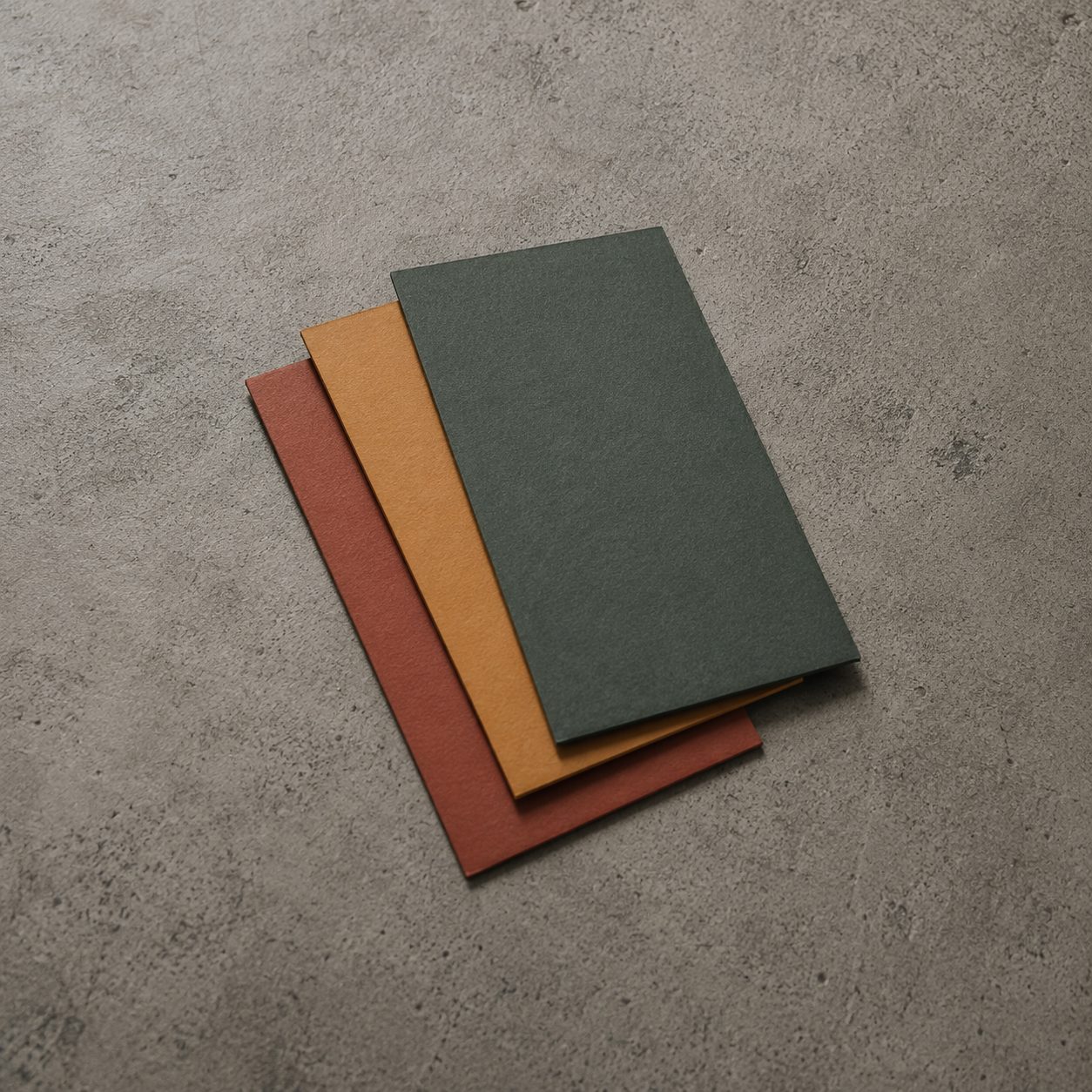 Tres cuadernos verde, ámbar y rojo sobre hormigón